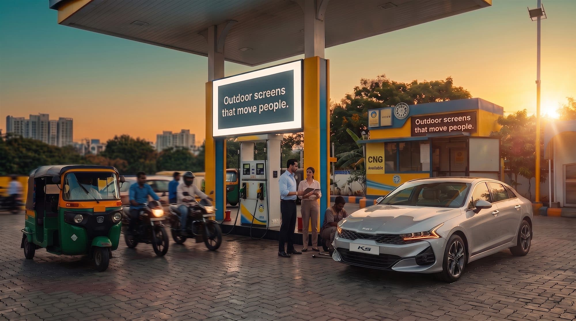Large DOOH advertising screen mounted under the canopy of an Indian petrol pump at sunset, with a customer, attendant, motorcycles and an auto-rickshaw moving through a network location ready to be monetised